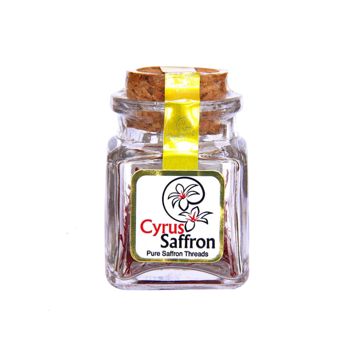 A small clear glass jar of Cyrus Saffron saffron threads with a cork stopper and a yellow ribbon, featuring a white label with red and black text.