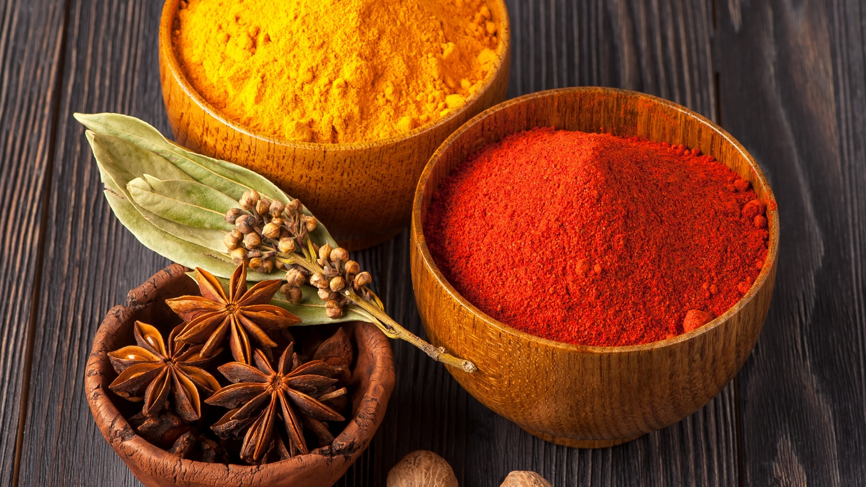 turmeric, paprika, star anise, and bay leaves in three wooden bowls