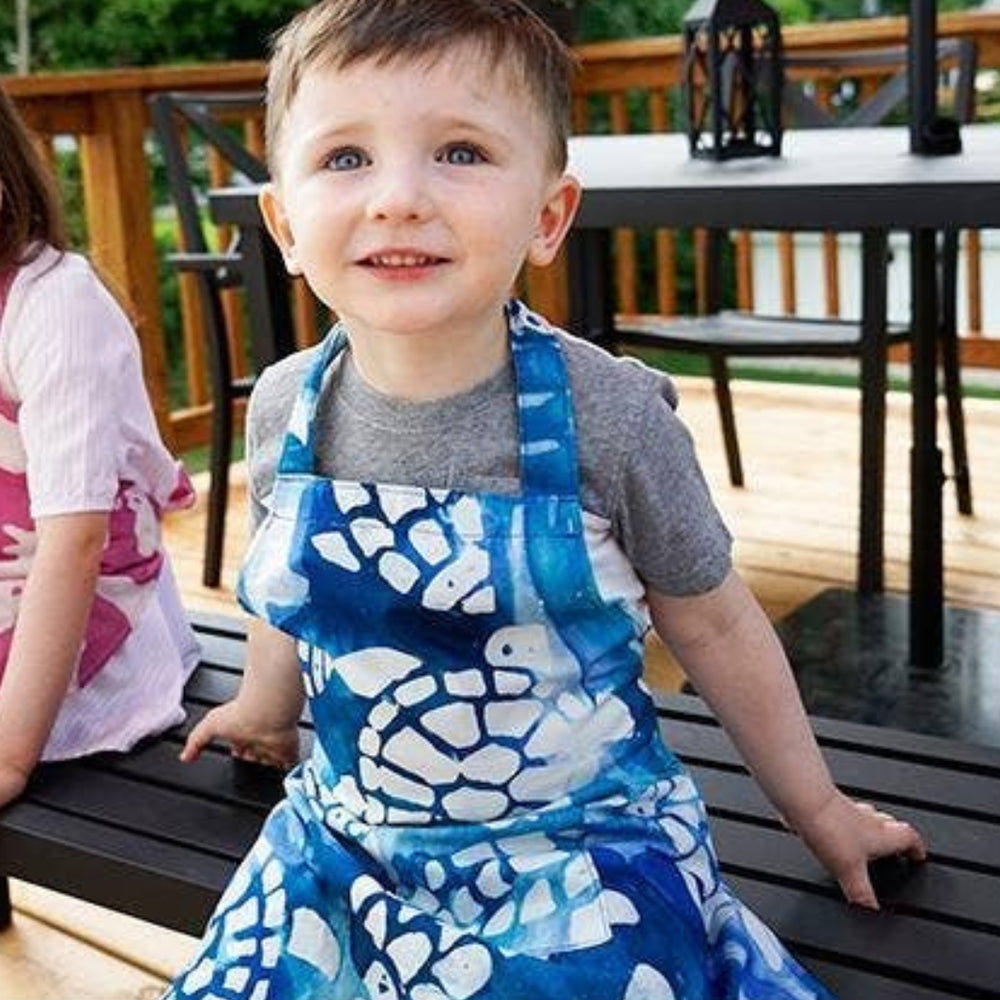 Kid Wearing an Apron with Playful White Turtles and Fish Swimming on an Ocean-Blue Background | Global Mamas® | Tiny Tastemakers @ Spice Craze®